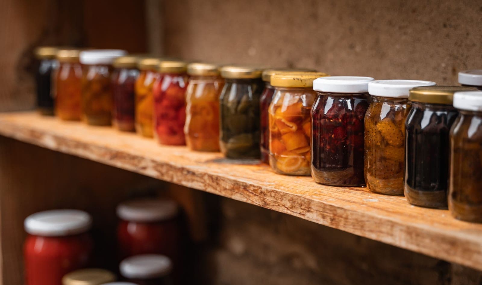 Row of homemade jam and preserve jars on a wooden shelf